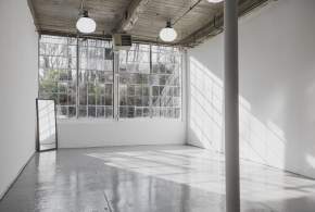 Large industrial windows letting in natural light in a white studio space with several overhead lights and a floor length mirror.