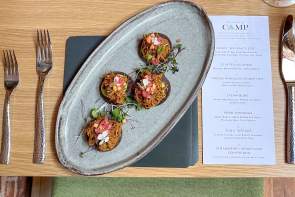 Overhead view of a plated dish of small bites and place setting with menu at CAMP.