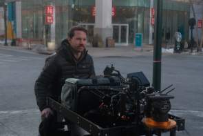 Man using a cart with wheels to transport camera and film equipment around a downtown environment.