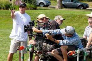 A group of four men on a film set using camera equipment and working together on a sunny day.
