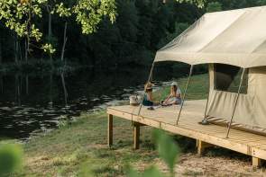 Two girls enjoy camping lakeside in a canvas tent at WYLDSTAY at Serenity Lake Farm in Fountain Inn, SC.