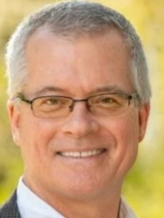 Closeup headshot for Dan Rogers focusing on his face from the neck up with a yellowish green blurred nature background
