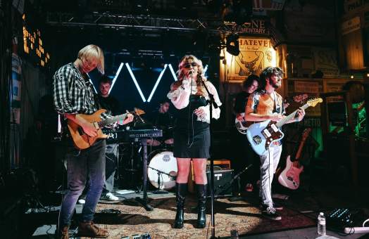 Small stage with five band members on guitars, drums, keyboard, and vocals at Swanson's Warehouse.