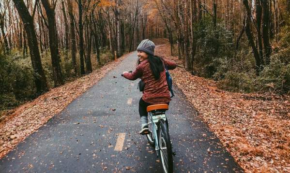 A person rides a bicycle down a leaf-strewn path surrounded by autumn trees.