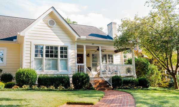 A cozy yellow house with a brick pathway, framed by a well-kept lawn and luscious hedges.