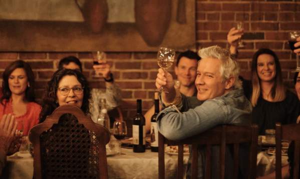 A lively group of people raising their glasses in a toast at Keipi, enjoying a toasting dinner inspired by Georgian traditions, with a table full of delicious food and wine.