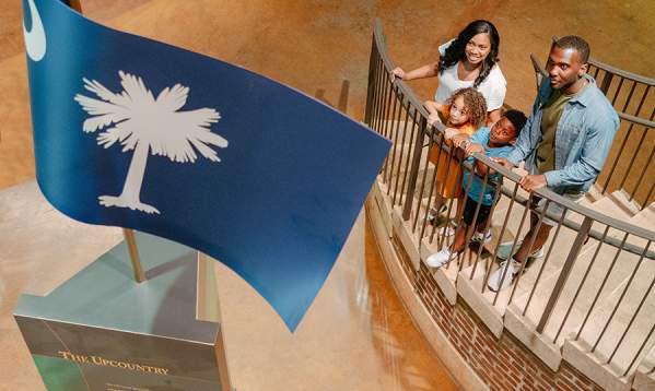 Family on stairs at the Upcountry History Museum admiring the South Carolina flag monument.