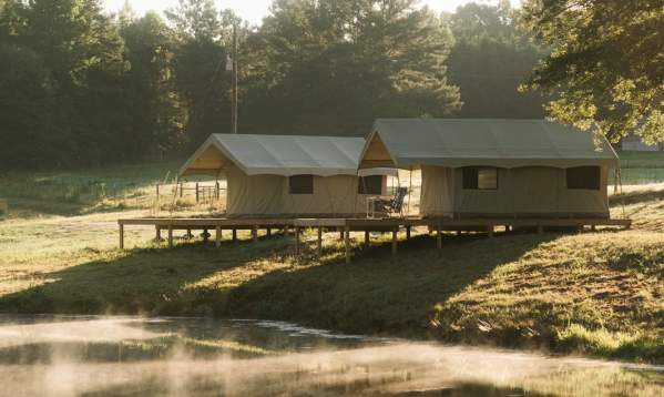 Two cozy Wyldstay cabins nestled by a serene lake, partially obscured by a light morning fog, creating a tranquil atmosphere.