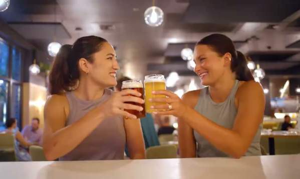 Two young women tapping glasses of beer together at a craft brewery in Greenville, SC.