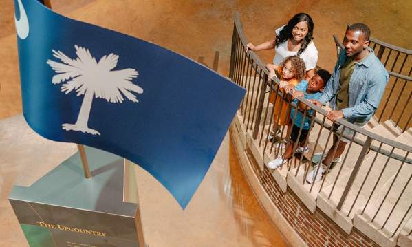 Family on stairs at the Upcountry History Museum admiring the South Carolina flag monument.