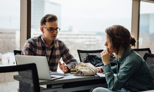 Two people talking and looking at a computer