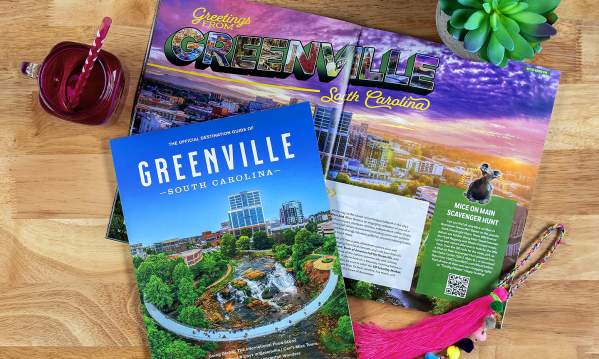 An opened copy of the 2024 Official Destination Guide of Greenville, SC next to a pink cup and plant.