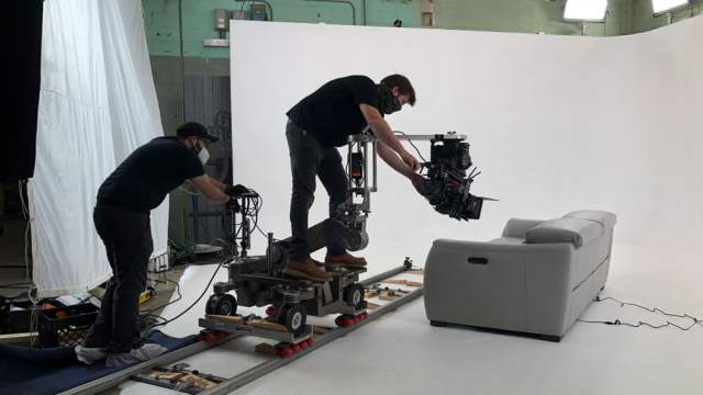 Cyclorama wall at CR8 with a bright white wall and bright overhead lights and a film crew recording footage of a grey couch