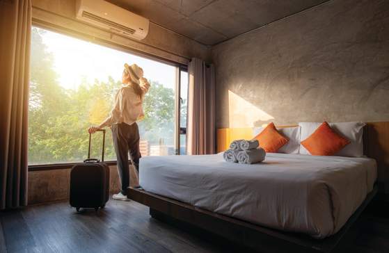 Woman looking out the window of her hotel room with her suitcase.