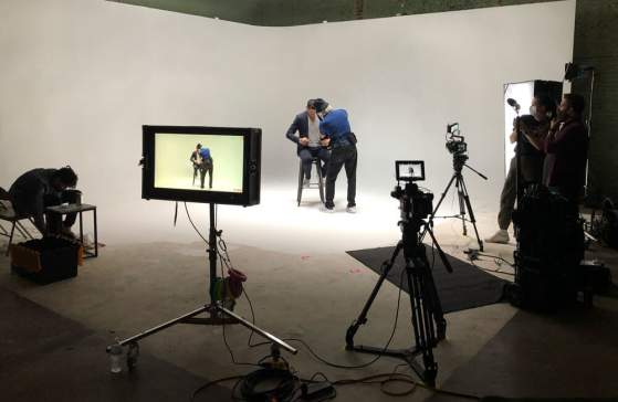 The Cyclorama wall at CR8, a blank white wall with a male actor on a stool and film equipment pointed at him getting ready to film underneath bright lights from above.