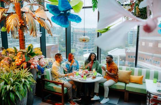 Group of four adults enjoying cocktails and food at Juniper, a uniquely decorated rooftop restaurant overlooking Downtown Greenville, SC.
