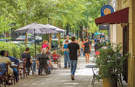 Groups of people dining and walking along tree-lined Main Street in Greenville, SC