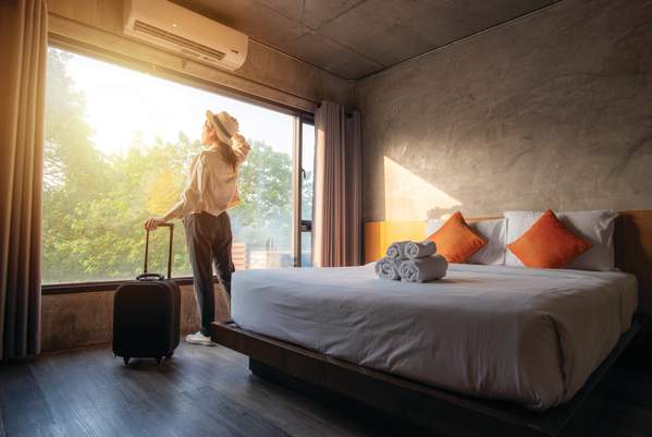 Woman looking out the window of her hotel room with her suitcase.