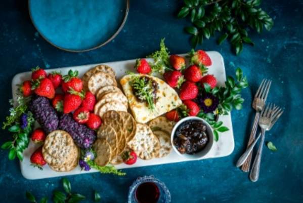 A fruit, cheese, and crackers plate sits atop a blue table with forks off to the side.