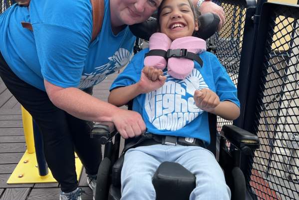 Woman smiling next to youth in wheelchair on accessible playground at The Children's Museum of the Upstate in Greenville, SC.