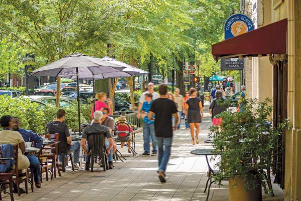 Groups of people dining and walking along tree-lined Main Street in Greenville, SC