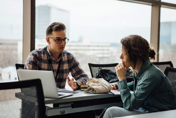 Two people talking and looking at a computer