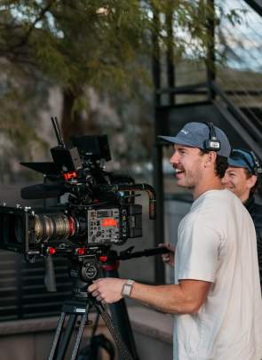 Two men filming with some trees and urban stair railing in the background and smiling while wearing headsets