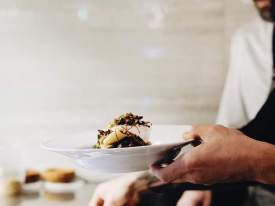 Topsoil Kitchen Chef Adam Cooke holding a plated dish and overseeing another dish