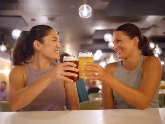 Two young women tapping glasses of beer together at a craft brewery in Greenville, SC.