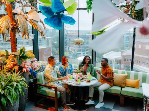 Group of four adults enjoying cocktails and food at Juniper, a uniquely decorated rooftop restaurant overlooking Downtown Greenville, SC.