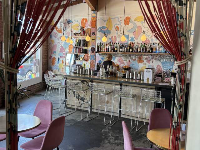 Interior image of Bar Margaret bar area with high-top stools and several low-top tables nearby with pink velvet chairs.