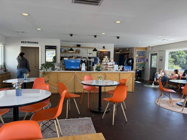 A modern and vibrant cafe interior with orange chairs, round tables, and a counter area with various items on display.