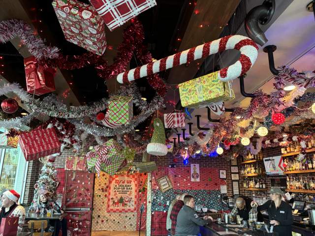 Wrapped presents and candy canes hang from the ceiling above a bar filled with patrons, all decorated for Christmas.