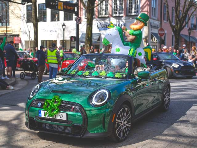 A festive green convertible in a St. Patrick's Day parade on Main Street, with an inflatable leprechaun riding a horse as part of its decorations.