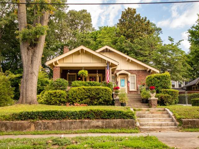 View of a quaint historic home from the street. There is lots of green grass and hedges.