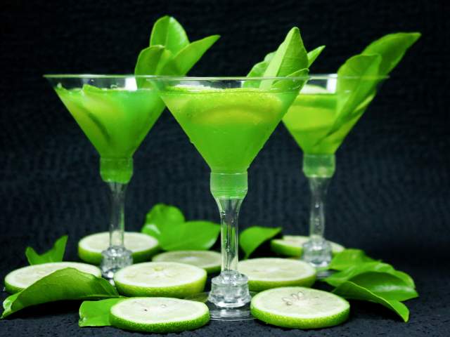 Three martinis with lime sit atop a black counter.