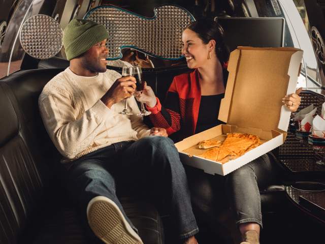 Man and woman enjoying a cheese pizza while in a limo