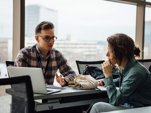 Two people talking and looking at a computer