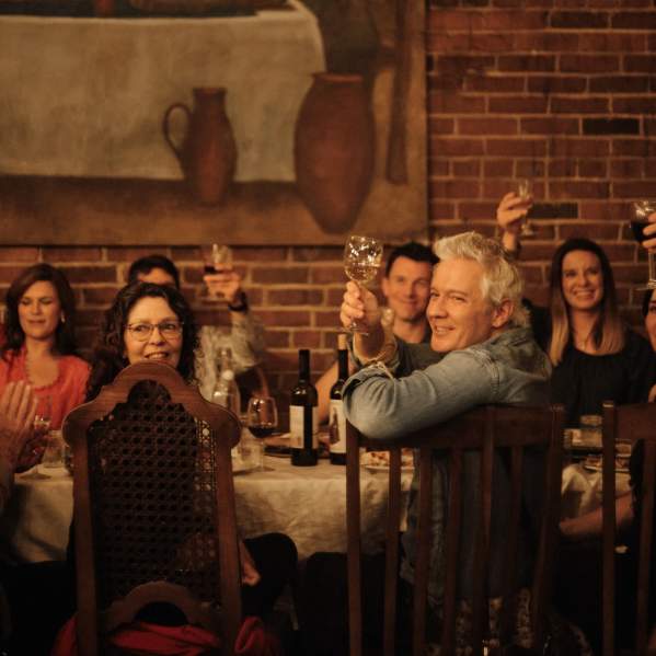A lively group of people raising their glasses in a toast at Keipi, enjoying a toasting dinner inspired by Georgian traditions, with a table full of delicious food and wine.