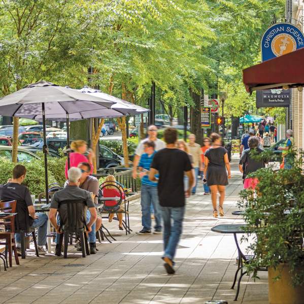 Groups of people dining and walking along tree-lined Main Street in Greenville, SC