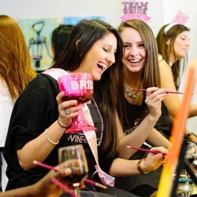 Two girls laughing while painting at Wine & Design