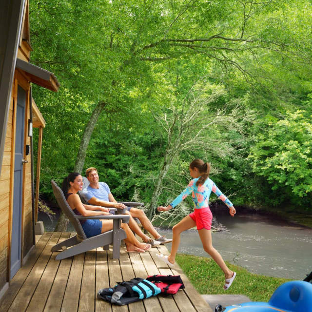 Family together sitting and running around on there cabin porch at the Saluda Outdoor Center