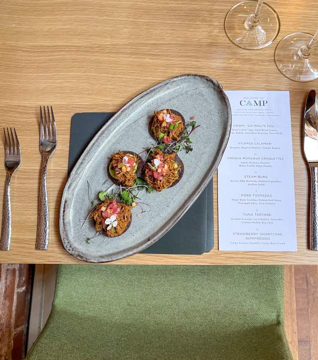 Overhead view of a plated dish of small bites and place setting with menu at CAMP.
