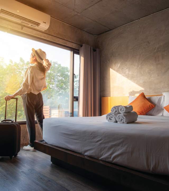 Woman looking out the window of her hotel room with her suitcase.