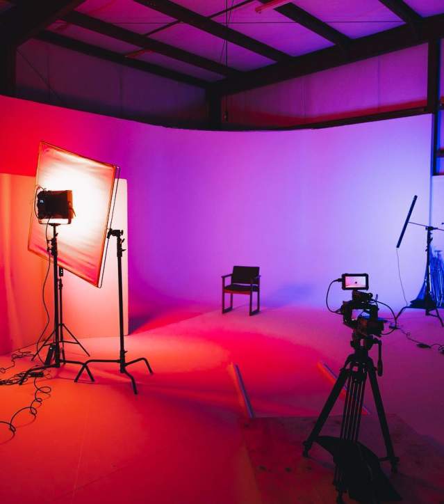 Red and purple lights creating a gradient background for photographers at the studio space at Kings Collective with camera equipment and a chair for a subject to sit.