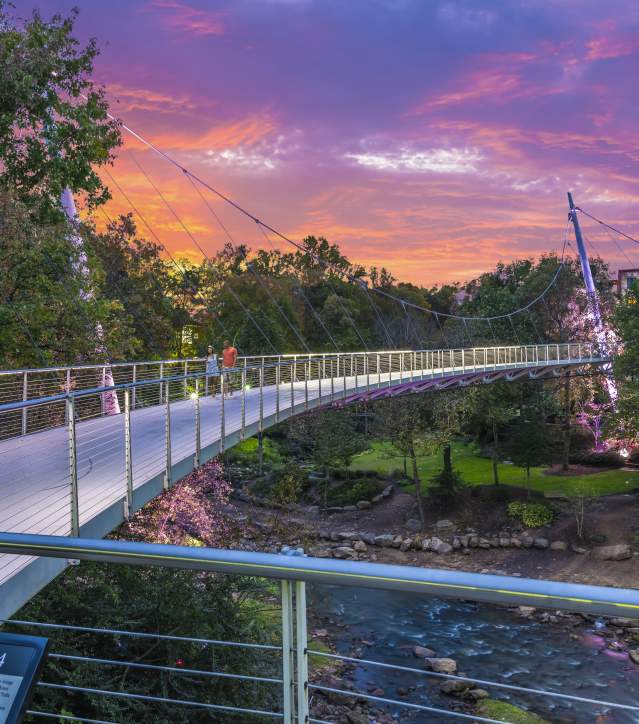A couple enjoys the sunset while walking across the Liberty Bridge at Falls Park on the Reedy.