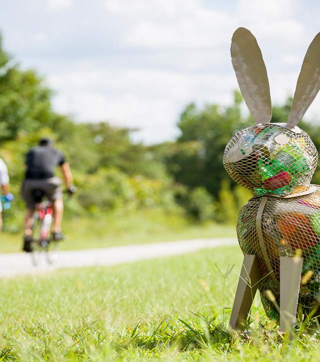 Statue of the recycle rabbit sitting in the grass near the pathway of the Swamp Rabbit Trail.