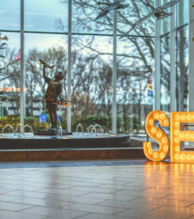 Light up marquee letters spelling S-E-C at GSP Int'l Airport in front of a fountain featuring a child holding a miniature airplane.