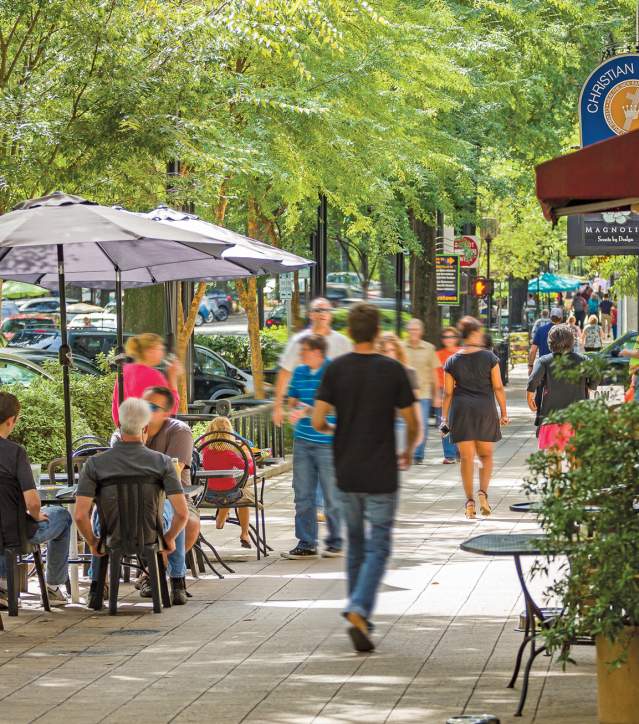 Groups of people dining and walking along tree-lined Main Street in Greenville, SC