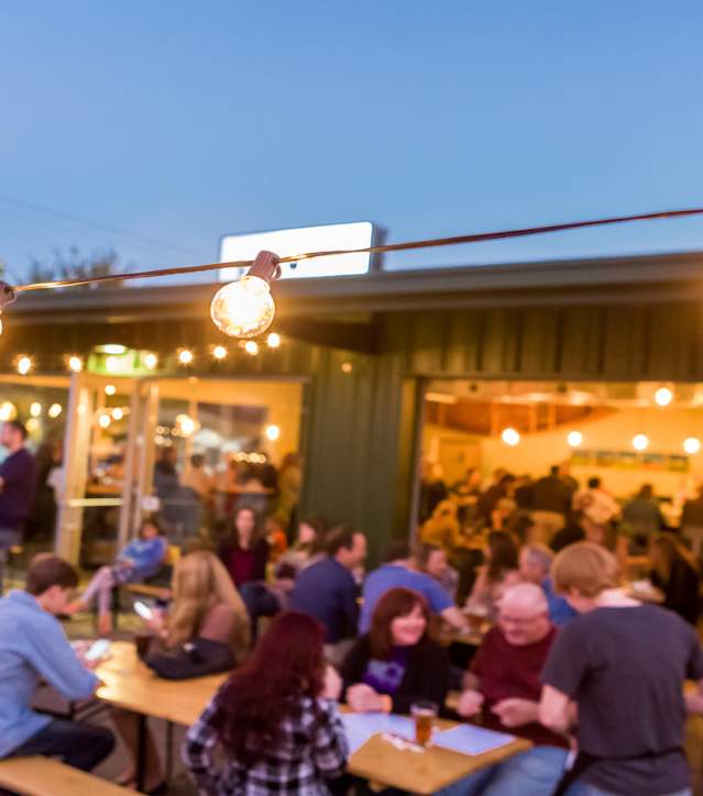 Customers sitting outside under rope lights while dining at the Sidewall Patio.